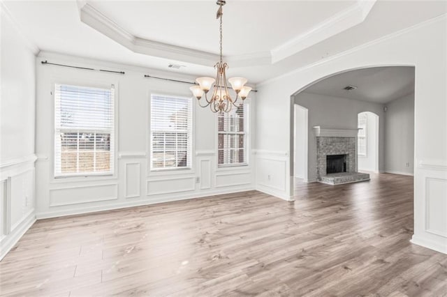 unfurnished dining area featuring visible vents, a fireplace with raised hearth, a raised ceiling, light wood-style flooring, and ornamental molding