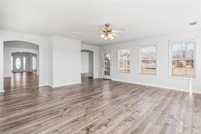 unfurnished living room with a healthy amount of sunlight, visible vents, arched walkways, and wood finished floors