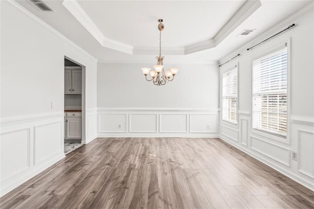 unfurnished dining area featuring visible vents, a raised ceiling, ornamental molding, wood finished floors, and a notable chandelier