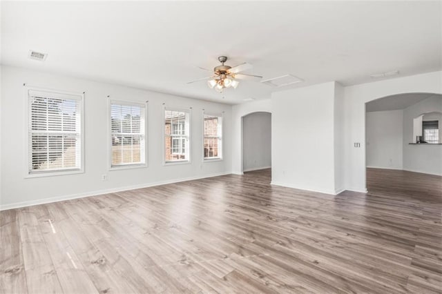 unfurnished living room with baseboards, visible vents, arched walkways, a ceiling fan, and light wood-type flooring