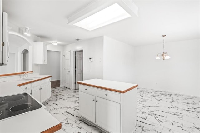 kitchen with marble finish floor, light countertops, hanging light fixtures, white cabinets, and a sink