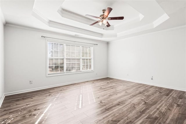 empty room with baseboards, a tray ceiling, wood finished floors, and crown molding