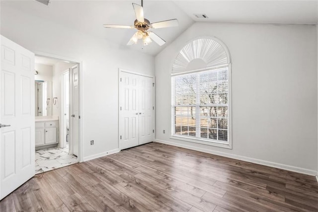 unfurnished bedroom featuring vaulted ceiling, ensuite bath, baseboards, and wood finished floors