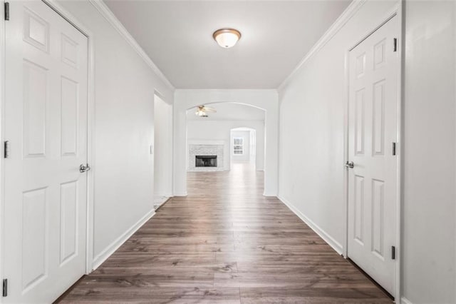 hall featuring baseboards, arched walkways, dark wood finished floors, and ornamental molding