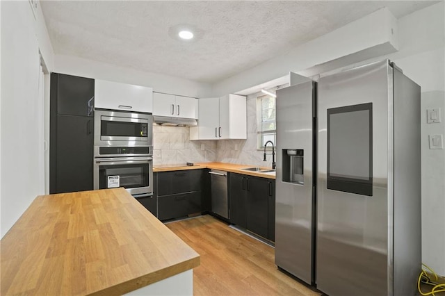 kitchen with backsplash, white cabinetry, stainless steel appliances, light wood-type flooring, and butcher block counters