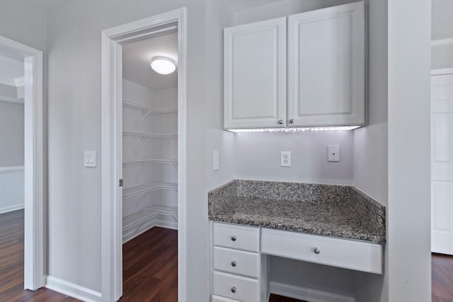 interior space with dark stone countertops, built in desk, white cabinets, and dark wood-type flooring