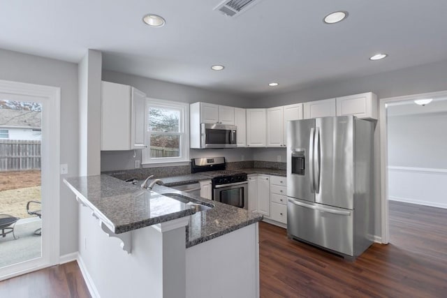 kitchen featuring kitchen peninsula, appliances with stainless steel finishes, white cabinets, and dark wood-type flooring