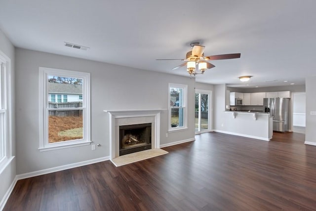 unfurnished living room with plenty of natural light, ceiling fan, and dark wood-type flooring