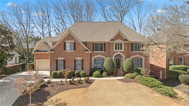 view of front of property featuring concrete driveway, a garage, brick siding, and roof with shingles