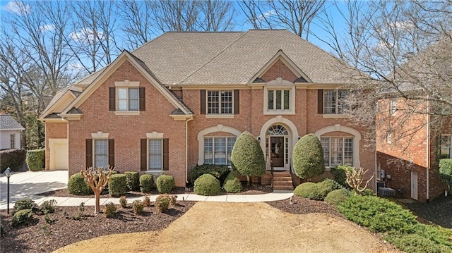 view of front of property featuring cooling unit, brick siding, roof with shingles, and concrete driveway