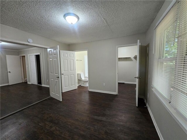 unfurnished bedroom featuring a closet, a walk in closet, a textured ceiling, and ensuite bath