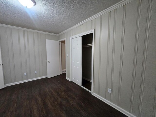 unfurnished bedroom with a textured ceiling, dark hardwood / wood-style flooring, a closet, and ornamental molding