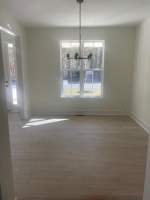 unfurnished dining area with a chandelier, baseboards, and wood finished floors