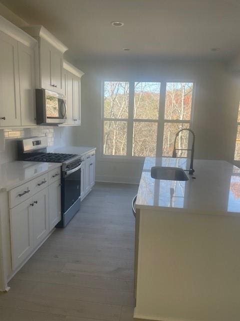 kitchen with a sink, backsplash, white cabinetry, appliances with stainless steel finishes, and light countertops