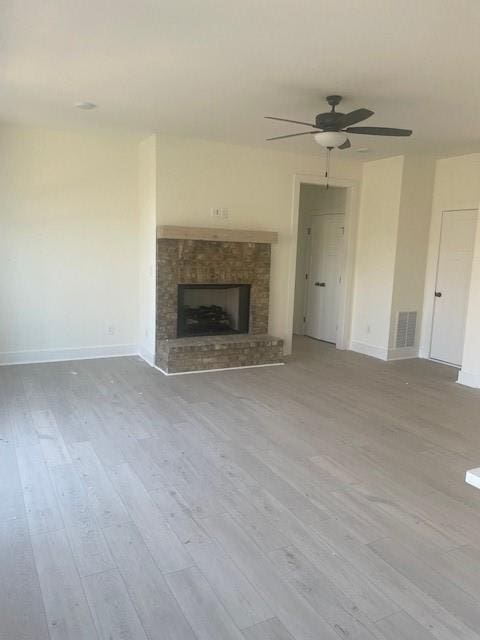 unfurnished living room featuring a ceiling fan, wood finished floors, visible vents, baseboards, and a fireplace with raised hearth