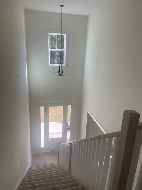 stairway with baseboards, an inviting chandelier, and a towering ceiling