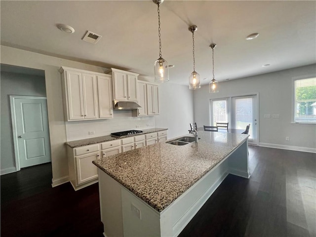 kitchen with pendant lighting, white cabinetry, a kitchen island with sink, light stone counters, and stainless steel gas stovetop