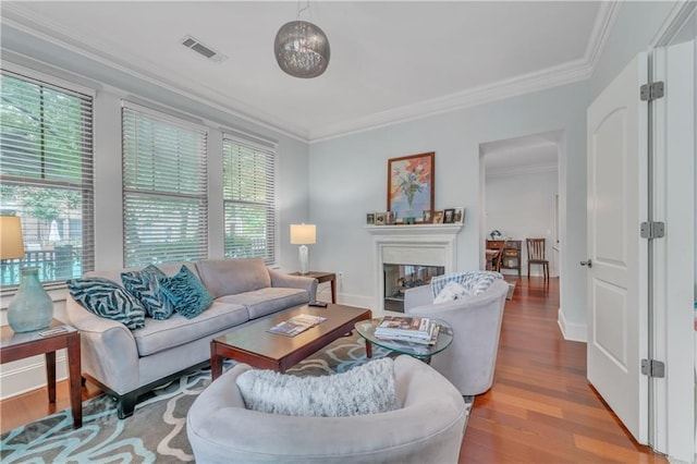 living area with wood finished floors, baseboards, visible vents, ornamental molding, and a glass covered fireplace