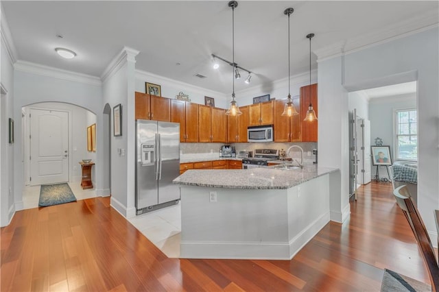 kitchen featuring stainless steel appliances, light stone counters, backsplash, kitchen peninsula, and decorative light fixtures