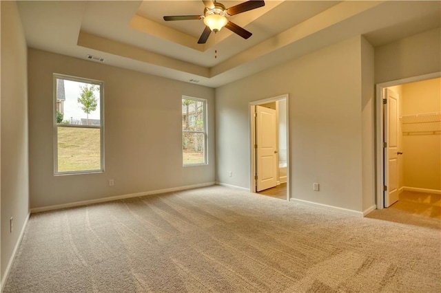 unfurnished bedroom featuring a walk in closet, a raised ceiling, light carpet, and multiple windows