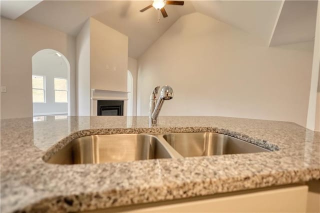 kitchen with light stone counters, ceiling fan, vaulted ceiling, and sink