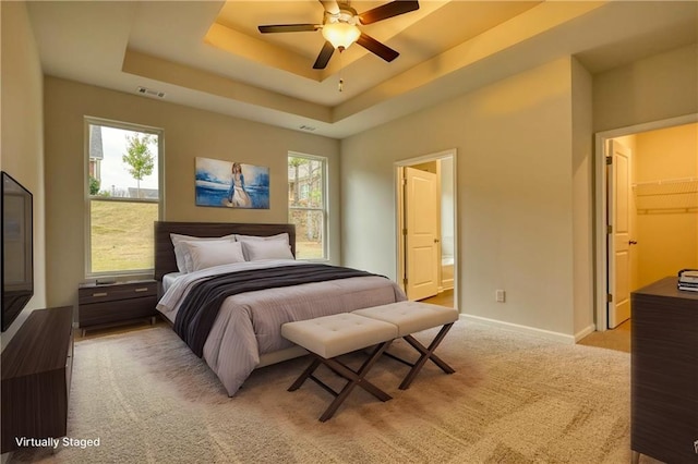 carpeted bedroom featuring a raised ceiling, a spacious closet, multiple windows, and ensuite bath