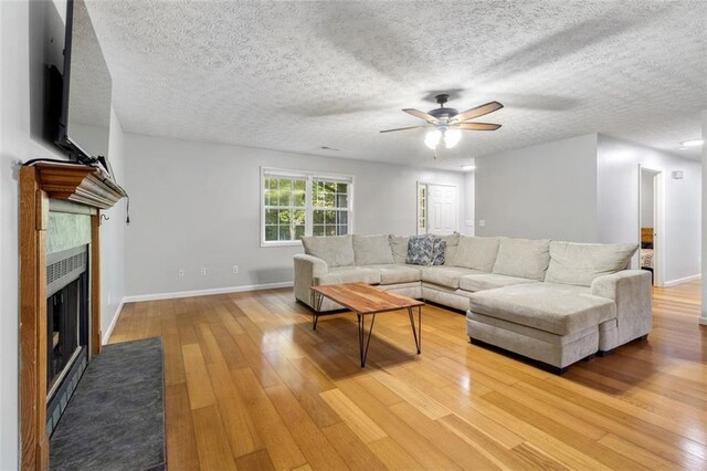 living room featuring a fireplace, a textured ceiling, light wood-type flooring, and ceiling fan