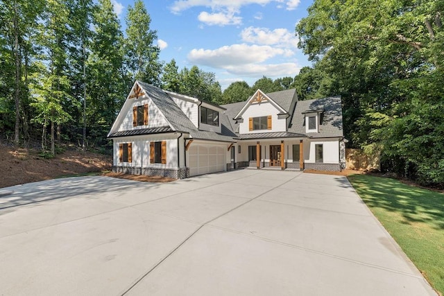 modern farmhouse style home featuring a standing seam roof, covered porch, an attached garage, and concrete driveway