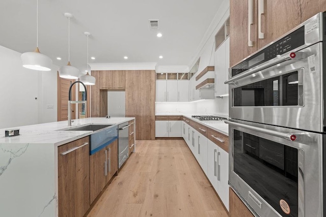 kitchen featuring appliances with stainless steel finishes, light wood-type flooring, a sink, light stone counters, and white cabinetry