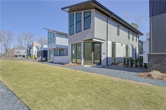 rear view of property featuring a residential view, a lawn, and stucco siding