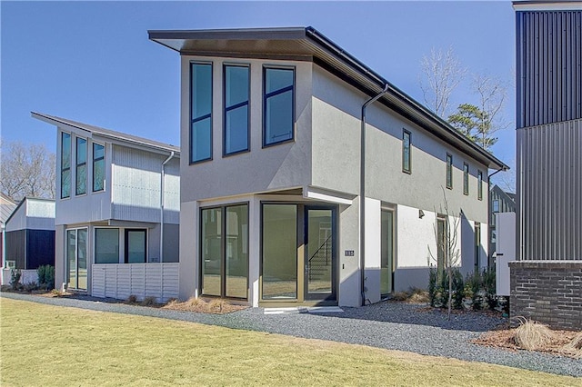 rear view of property featuring a lawn and stucco siding