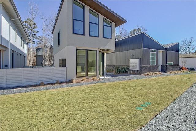 rear view of property with stucco siding, fence, and a yard