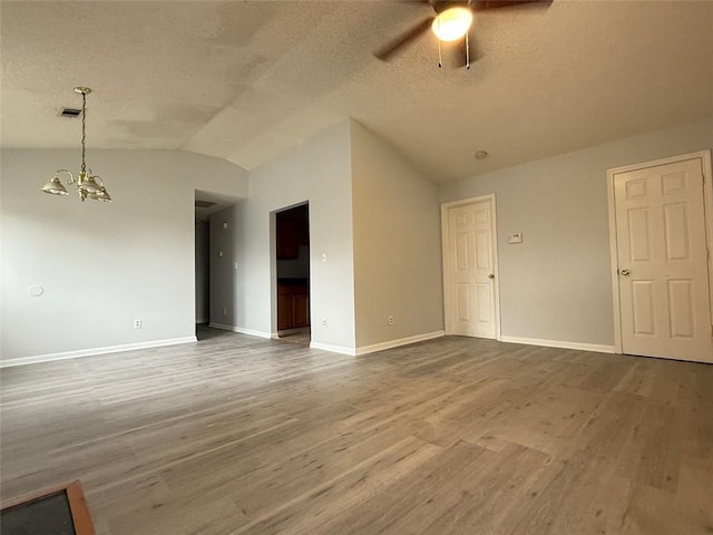 unfurnished room with a textured ceiling, ceiling fan with notable chandelier, wood-type flooring, and lofted ceiling