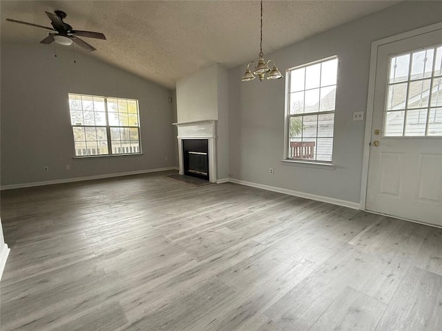 unfurnished living room with lofted ceiling, ceiling fan with notable chandelier, light hardwood / wood-style floors, and a textured ceiling