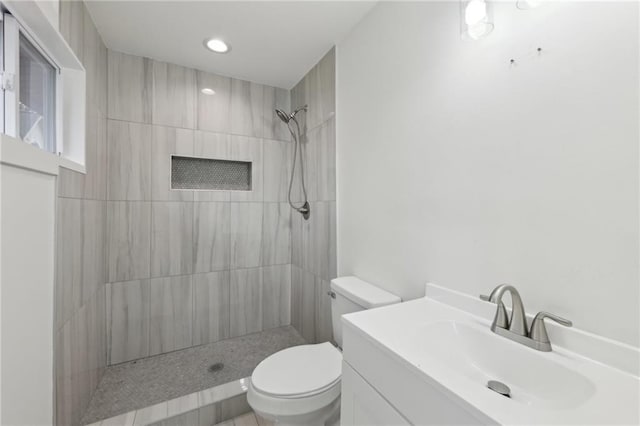 bathroom featuring toilet, tiled shower, and vanity