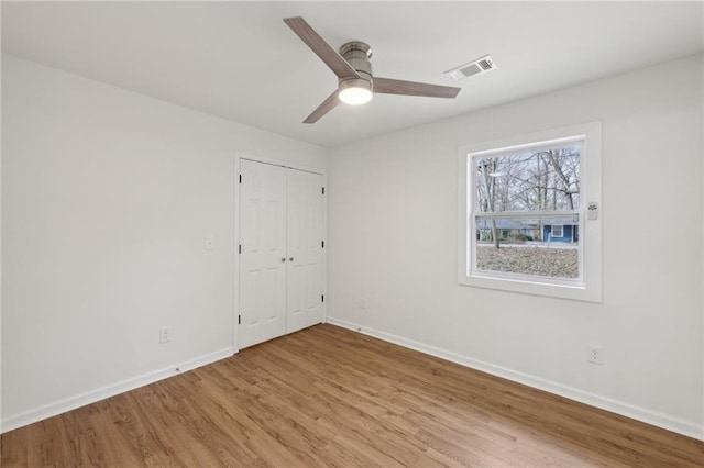 spare room featuring light wood finished floors, baseboards, visible vents, and ceiling fan