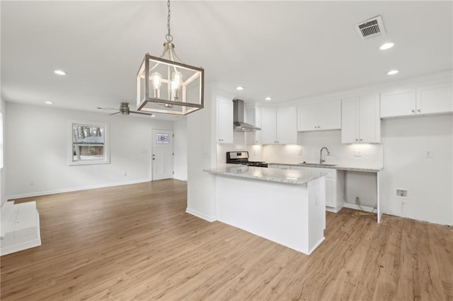 kitchen with stainless steel stove, visible vents, white cabinetry, a sink, and wall chimney exhaust hood