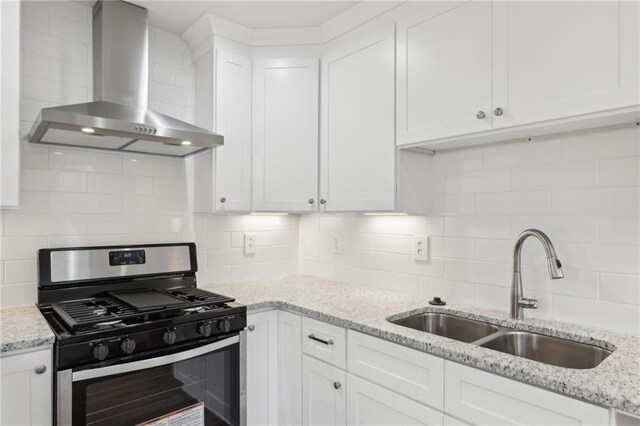 kitchen with backsplash, white cabinetry, a sink, wall chimney range hood, and stainless steel gas range oven