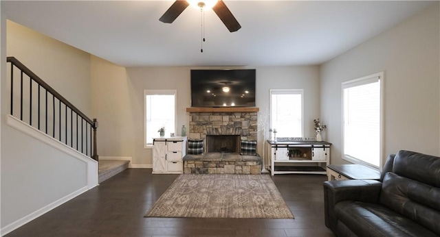 living room with a stone fireplace, ceiling fan, and dark wood-type flooring