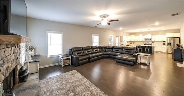 living room featuring a stone fireplace, ceiling fan, and dark hardwood / wood-style flooring