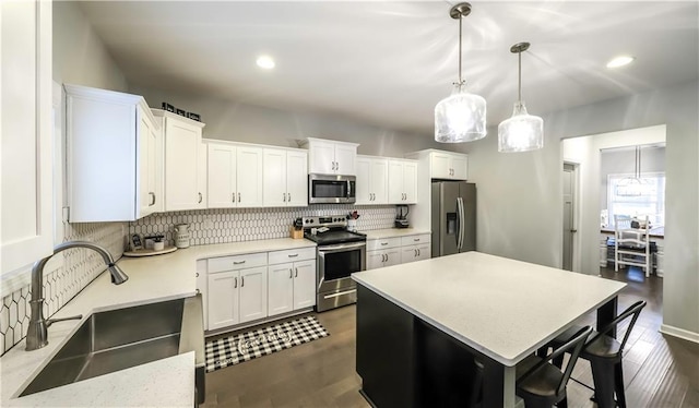 kitchen featuring white cabinets, sink, hanging light fixtures, a kitchen island, and stainless steel appliances