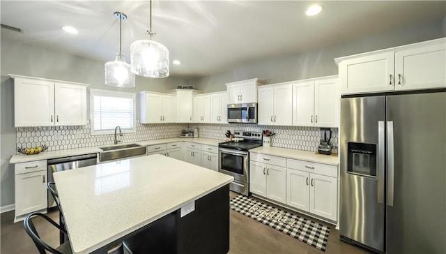 kitchen featuring white cabinetry, sink, decorative light fixtures, a kitchen island, and appliances with stainless steel finishes