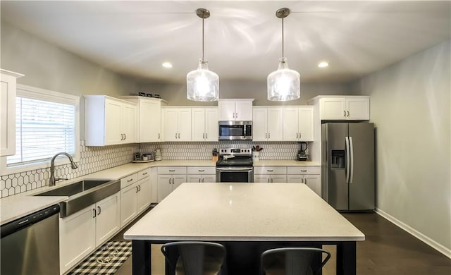 kitchen with sink, hanging light fixtures, stainless steel appliances, a kitchen island, and white cabinets