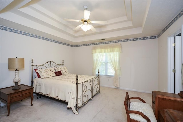 carpeted bedroom with a raised ceiling and ceiling fan