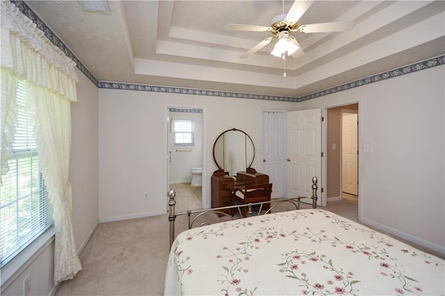 carpeted bedroom featuring ensuite bathroom, a raised ceiling, and ceiling fan