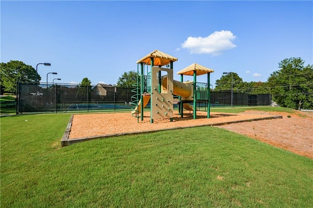 view of playground featuring a lawn and tennis court