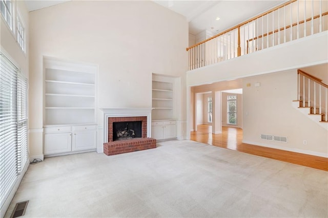 unfurnished living room with hardwood / wood-style flooring, built in features, a towering ceiling, and a fireplace