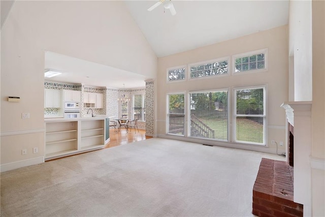 unfurnished living room featuring high vaulted ceiling, ceiling fan with notable chandelier, sink, a fireplace, and light colored carpet