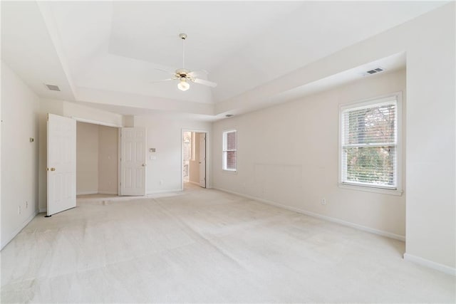 unfurnished room featuring a raised ceiling, ceiling fan, and light colored carpet