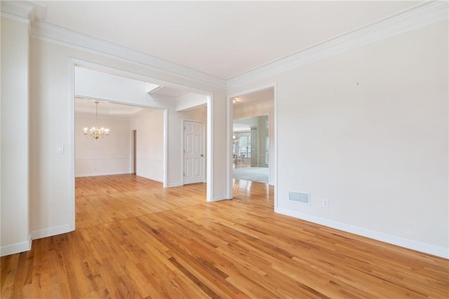 spare room with a notable chandelier, ornamental molding, and light hardwood / wood-style flooring